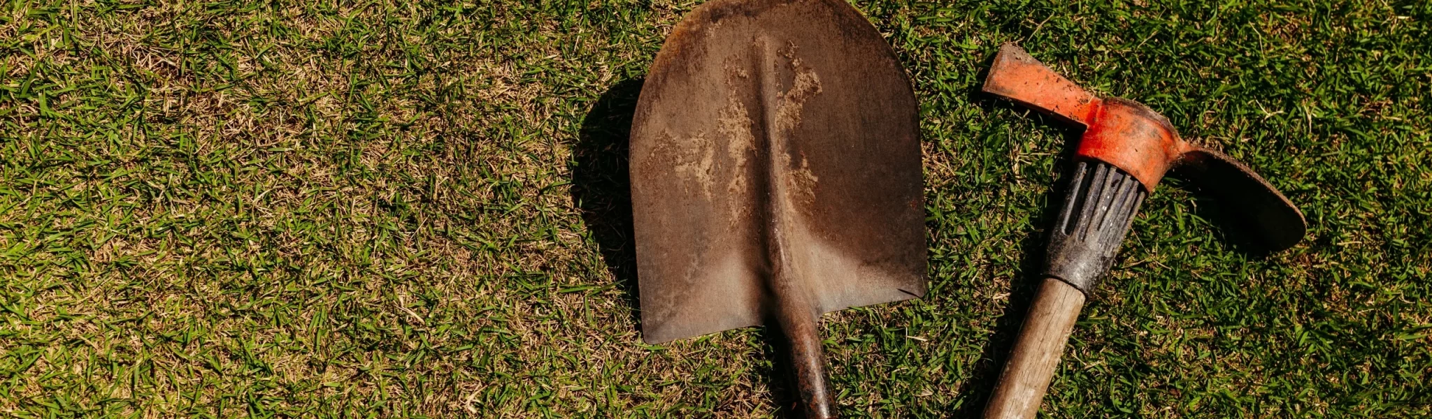 A shovel and pickaxe bought from a landscaping supplier lying on the grass